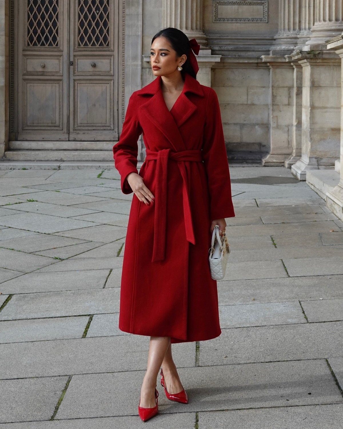 Pat Chaveesak in a red wool coat in front of Parisian stone architecture, full length shot, natural daylight, self shot